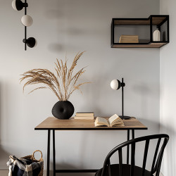Op een bureau van licht hout staat een moderne bureaulamp van zwart metaal met een lamphuis in de vorm van een witte bol.